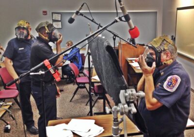 Three firefighters stand in front of microphones wearing full face respirators recording lines for a 3D scenario for the Fire Hero Learning Network