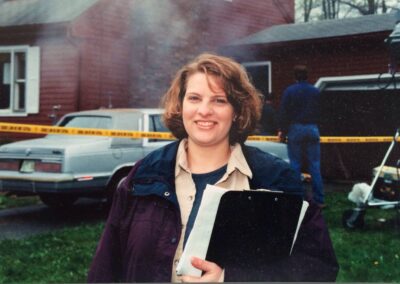 Cathy Dipierro stands in front of a red, cape-style house with smoke coming out of the door during the video shoot for interFIRE VR